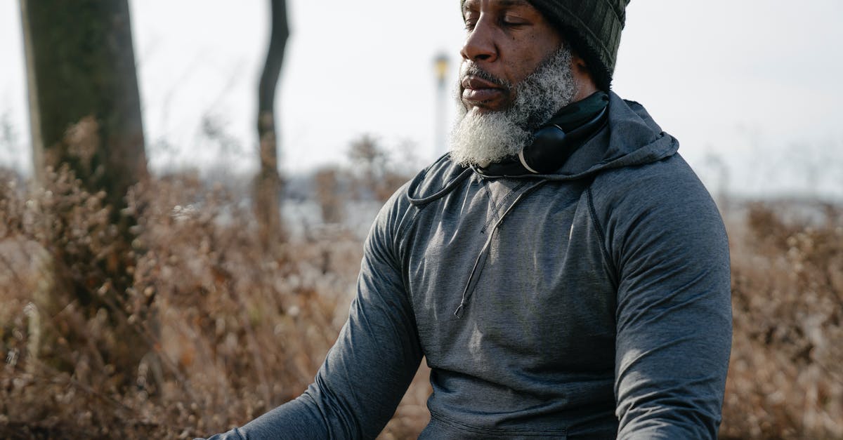 Silent / quiet luggage, trolley, on wheels [closed] - Bearded African American male in warm activewear and knitted hat sitting and meditating with closed eyes in autumn nature