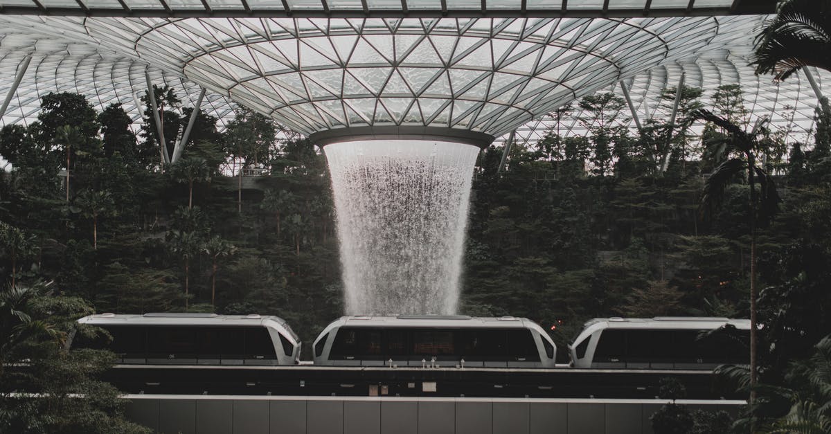 Singapore Changi Airport: Is Terminal 4 connected Airside to other terminals - Contemporary rail link train going under indoors waterfall streaming from creative glass ceiling in Jewel Changi Airport in Singapore