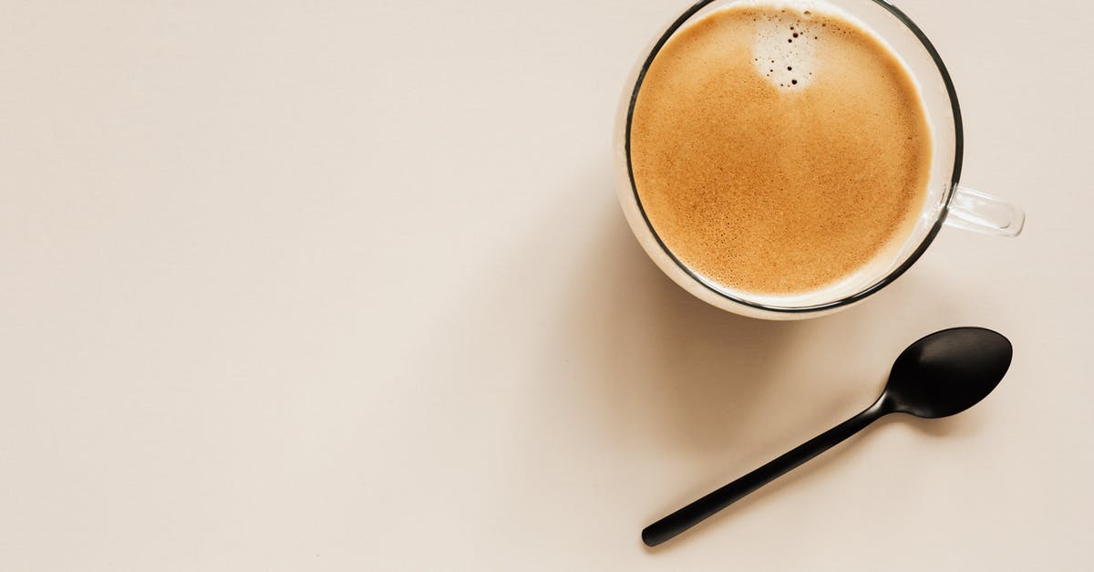 Single-entry visa from the Italian embassy - Top view of glass of aromatic light brown coffee with foam and small bubbles on top near metal spoon on beige surface