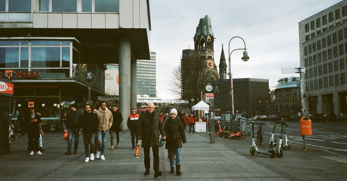 Single-ticket trip in Brandenburg, Germany - Full body of anonymous people in warm clothes walking on paved pedestrian street near modern buildings and ancient Kaiser Wilhelm Memorial Church in Berlin