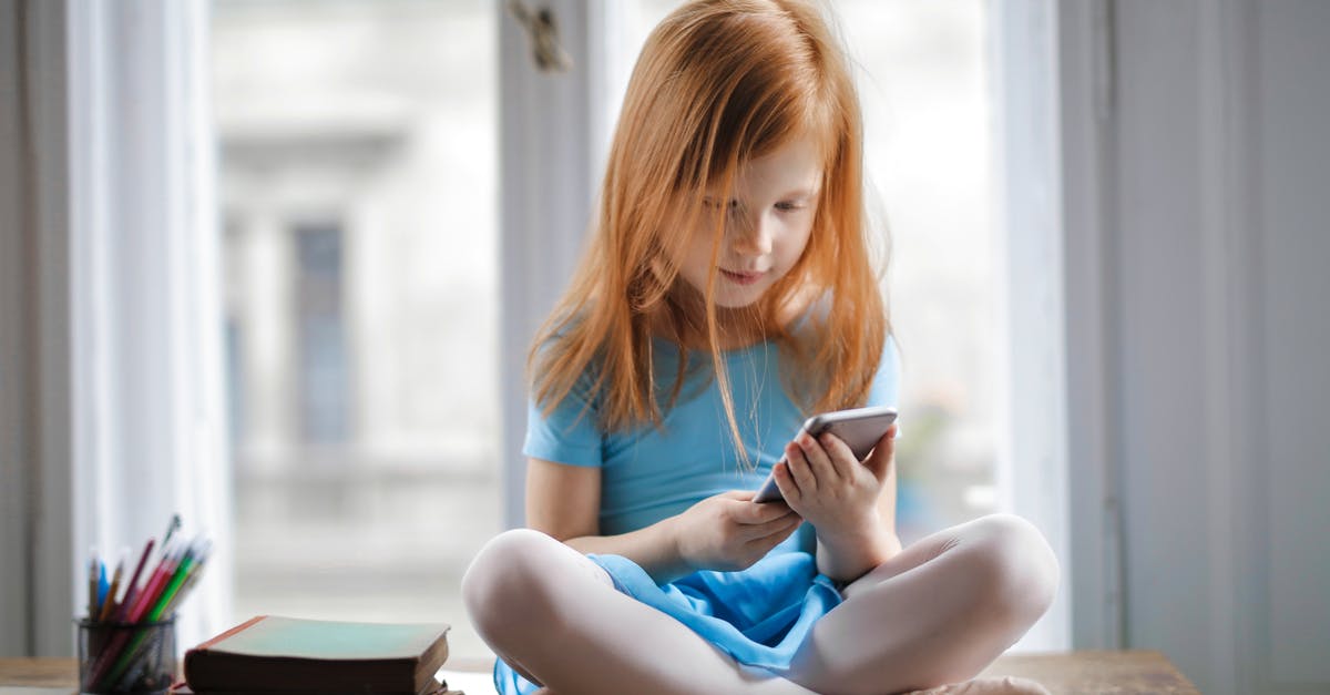 Small Mexican hotel would not take credit card to book room - Red haired charming schoolgirl in blue dress browsing smartphone while sitting on rustic wooden table with legs crossed beside books against big window at home