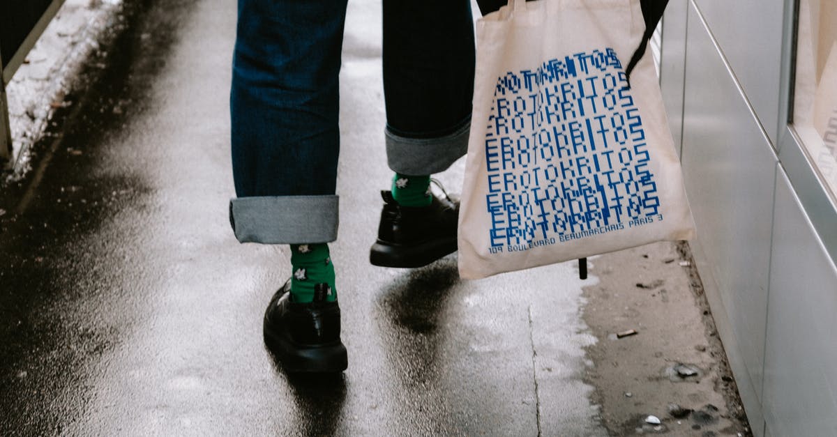 Small umbrella in the carry-on bag? - Person in Blue Denim Jeans and Black Shoes Holding Tote Bag and Black Umbrella