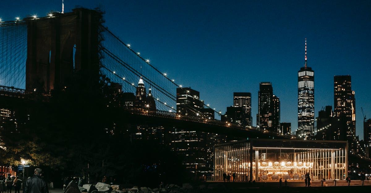 Social/nightlife in the US (NYC, Boston, Chicago) through hostels [closed] - Glowing city lights on high rise buildings and suspension bridge over river with sidewalk on embankment