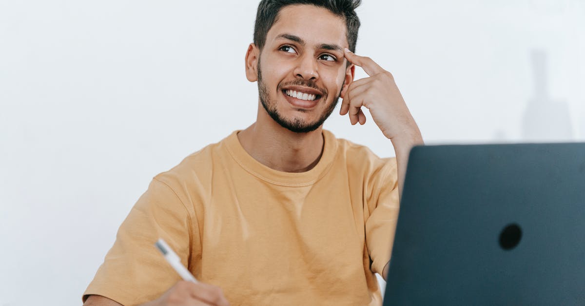 Software, Apps, Online Planner for planning backup route - Smiling young bearded Hispanic male entrepreneur thinking over new ideas for startup project and looking away dreamily while working at table with laptop and taking notes in notebook