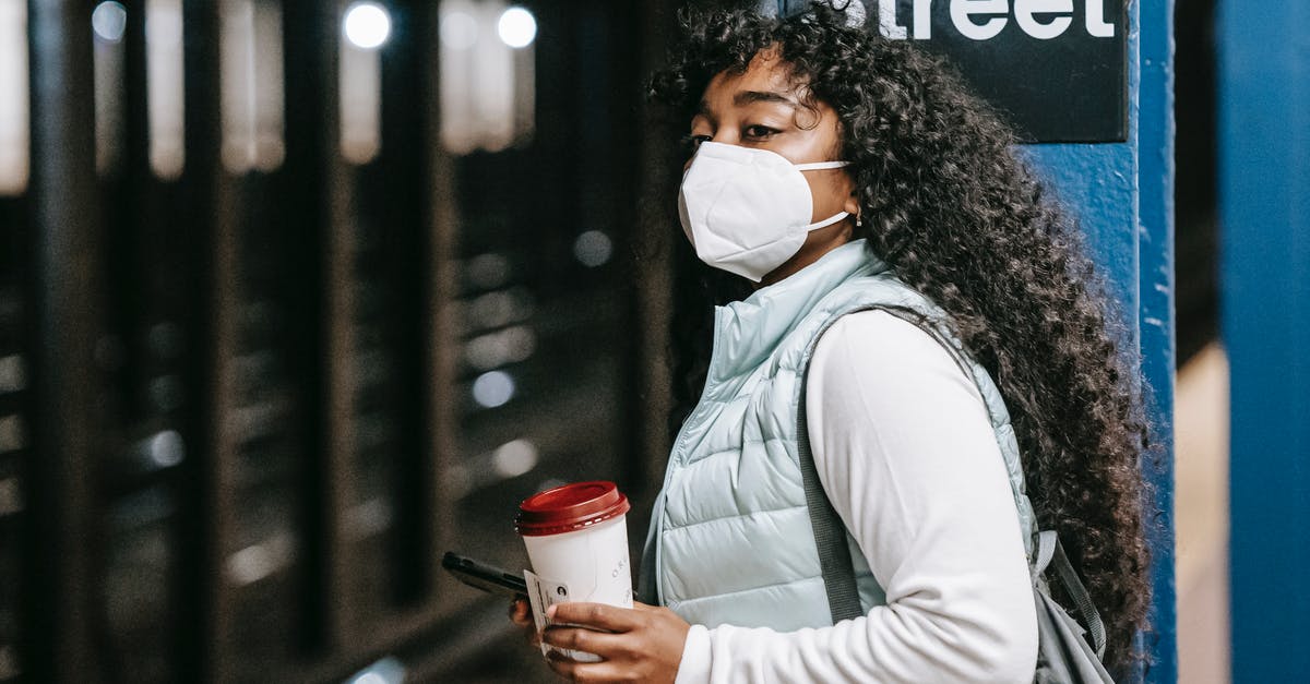 South African passport but British citizen living in the US planning a trip back to the UK - Black woman in respirator waiting for train in subway