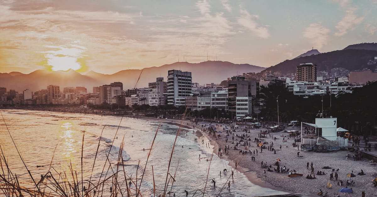 South African passport holder traveling from South Africa, via Luanda, Angola to Rio de Janeiro, Brazil - Rio de Janeiro coastline with modern buildings and people resting on sandy beach near calm ocean in evening time with sun setting over mountains