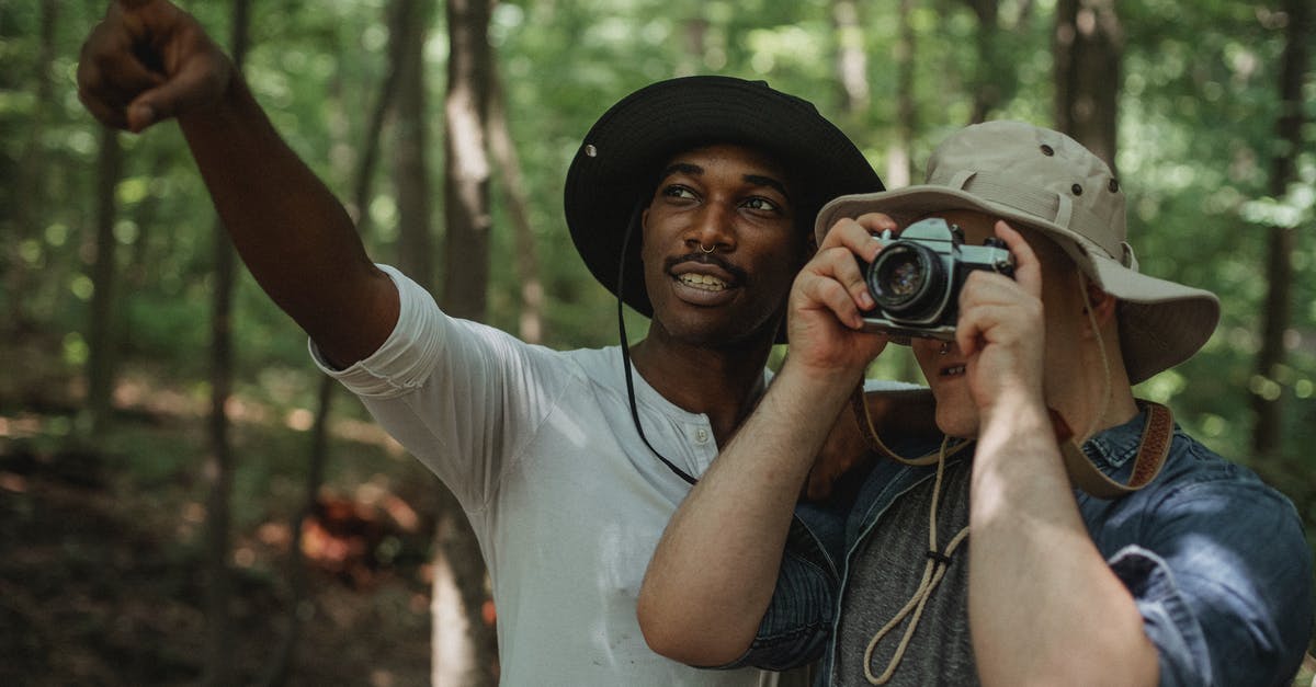 Spending a night in Minsk and continuing my journey using my Fan ID - Young black male traveler indicating with finger near anonymous best friend taking photo on camera in woods