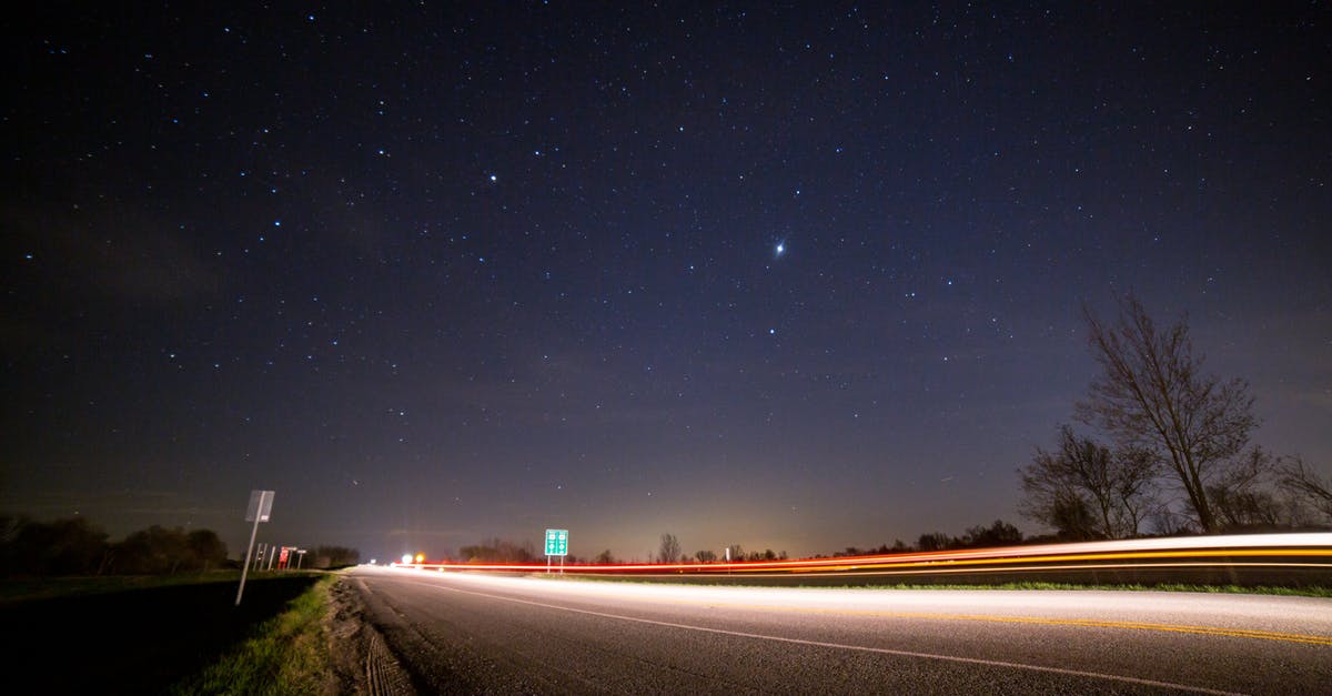 Star Alliance - direct routes - From below of glowing asphalt road with fence near trees and road signs under picturesque night sky with luminous stars at sundown