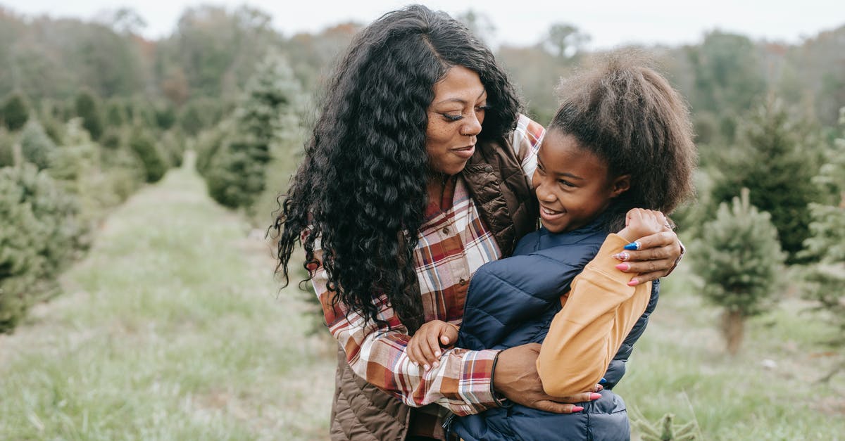 Staying in Hostels in December in Europe [closed] - Cheerful African American mum cuddling child while standing close among rows of Christmas trees