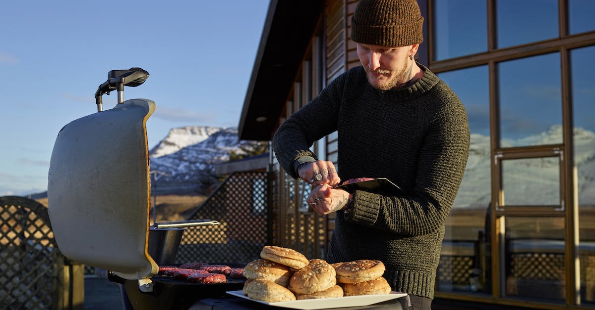 Steak house in Amsterdam? - Concentrated young male in warm outfit preparing delicious grilled meat while standing against cozy house in winter day