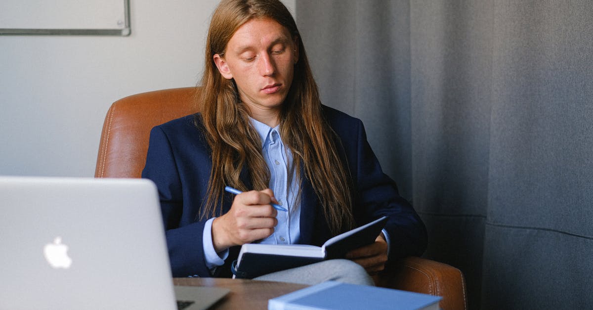 Strategy for cruise tickets: book now or last minute? - Pensive androgynous businessman in formal suit sitting at table with laptop and book and taking notes in notebook in workspace
