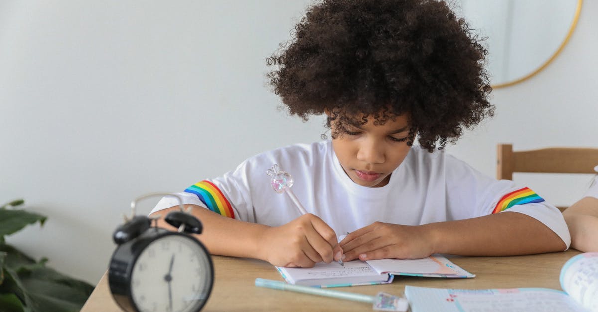 Subclass 600 Processing time changed - Concentrated African American child writing in notebook while studying at desk with alarm clock at home