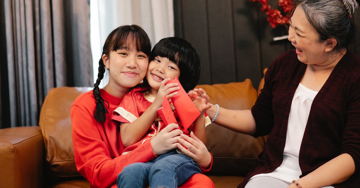 Suggestions for 15 year old ( child / teen ) travelling alone - Smiling ethnic female adolescent embracing sibling with red pocket against grandma on couch during New Year holiday at home