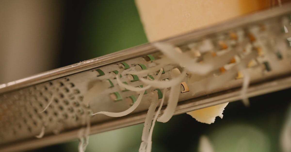 Suitcases: hard or soft?  Canvas, polycarbonate or something else? - Closeup of tasty hard cheese grating on narrow stainless grater against blurred kitchen background