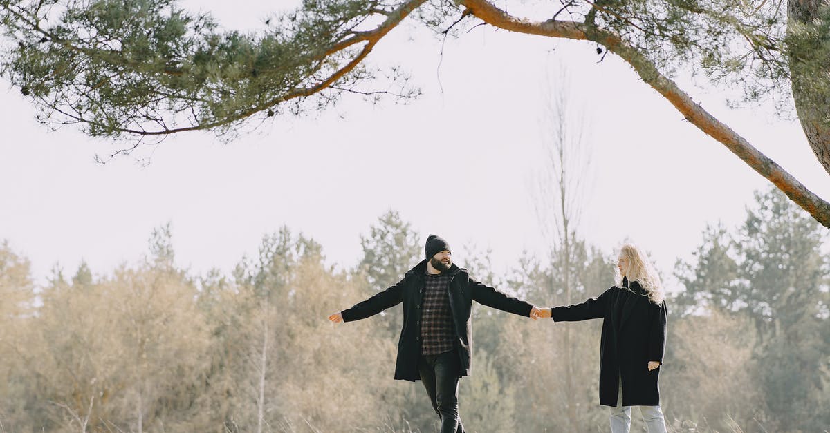 Supplies and support on a long-distance walk - Full body happy lovers in warm casual coats holding hands while spending time together in autumn park looking at each other