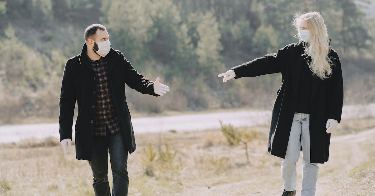 Supplies and support on a long-distance walk - Casual couple in warm coats and protective masks latex gloves looking pulling hands to each other during weekend stroll together