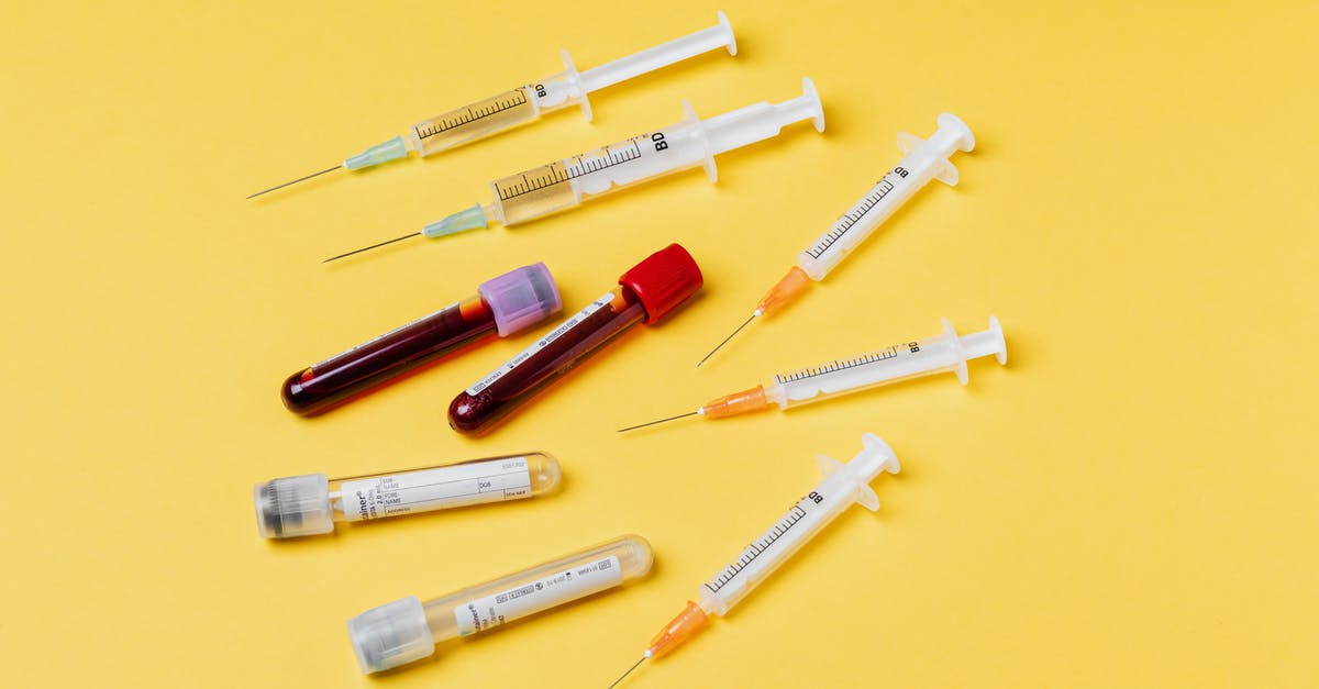Supplying your own needle for Blood test for a Kurdistan residency permit - From above composition with medical syringes of different sizes arranged with test tubes filled with blood samples placed on yellow surface