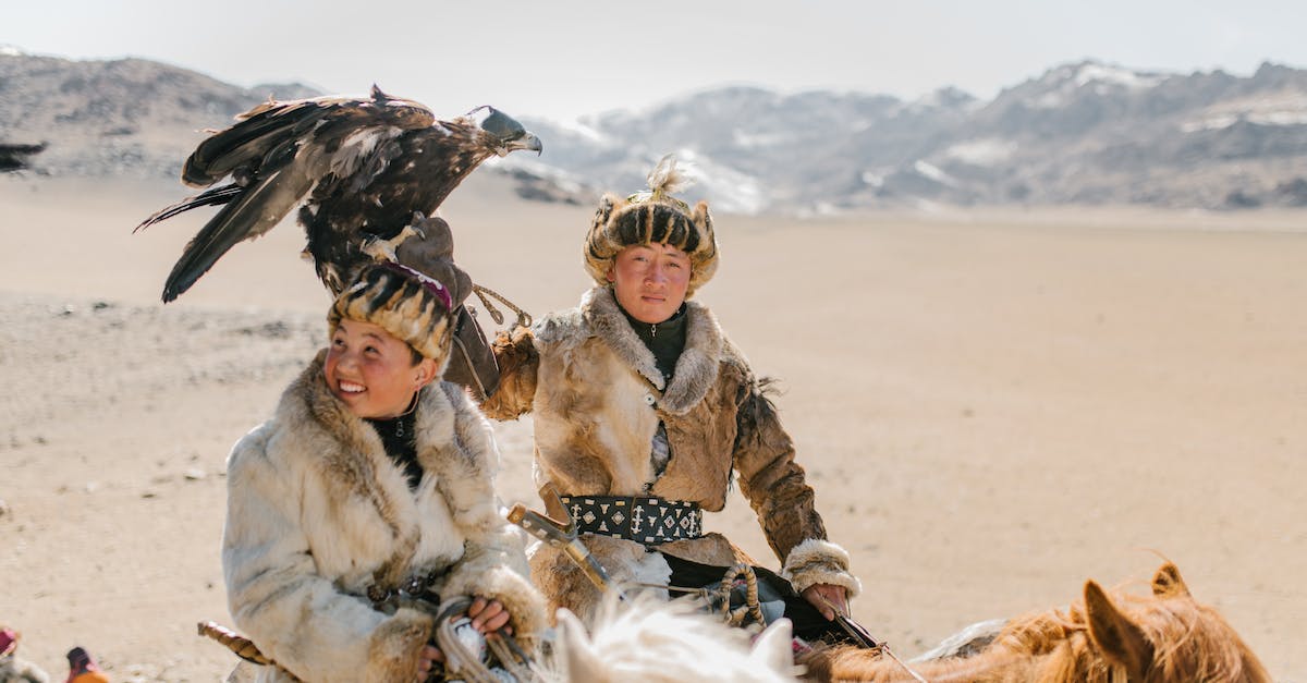Sustainable hunting in South-East Asia - Positive Mongolian eagle hunters riding horses on mountainous terrain