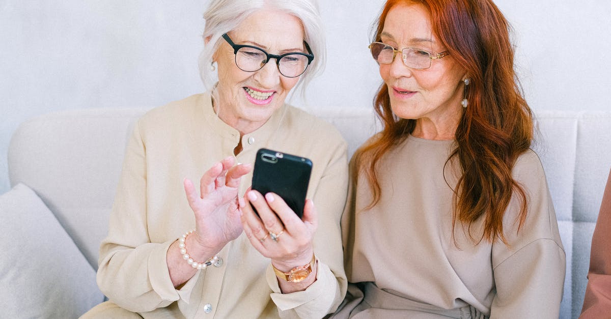 Tax-free shopping in Faroe Islands - Happy elderly elegant trendy women looking at screen of mobile phone and shopping online while resting on sofa