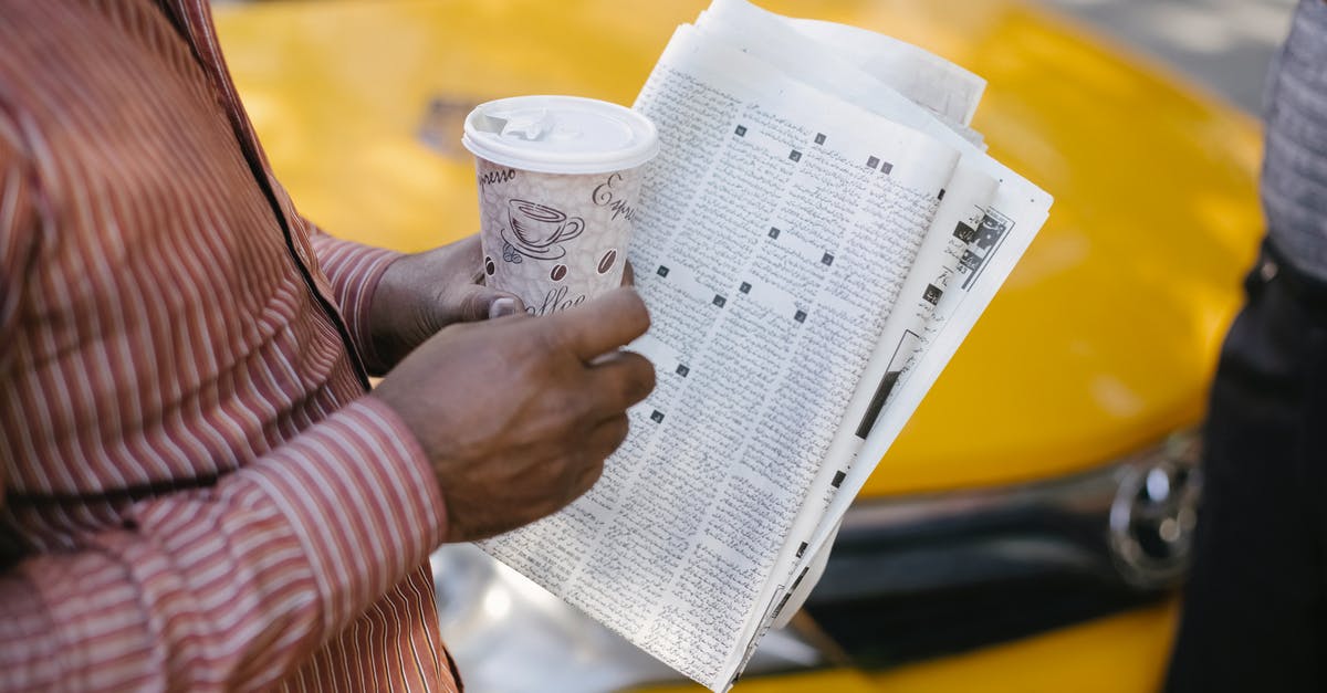 Taxi from Pistoolhaven to Luxemburgweg Europoort in the Netherlands - From above side view of crop anonymous ethnic male cab driver with coffee to go and newspaper talking to coworker on street