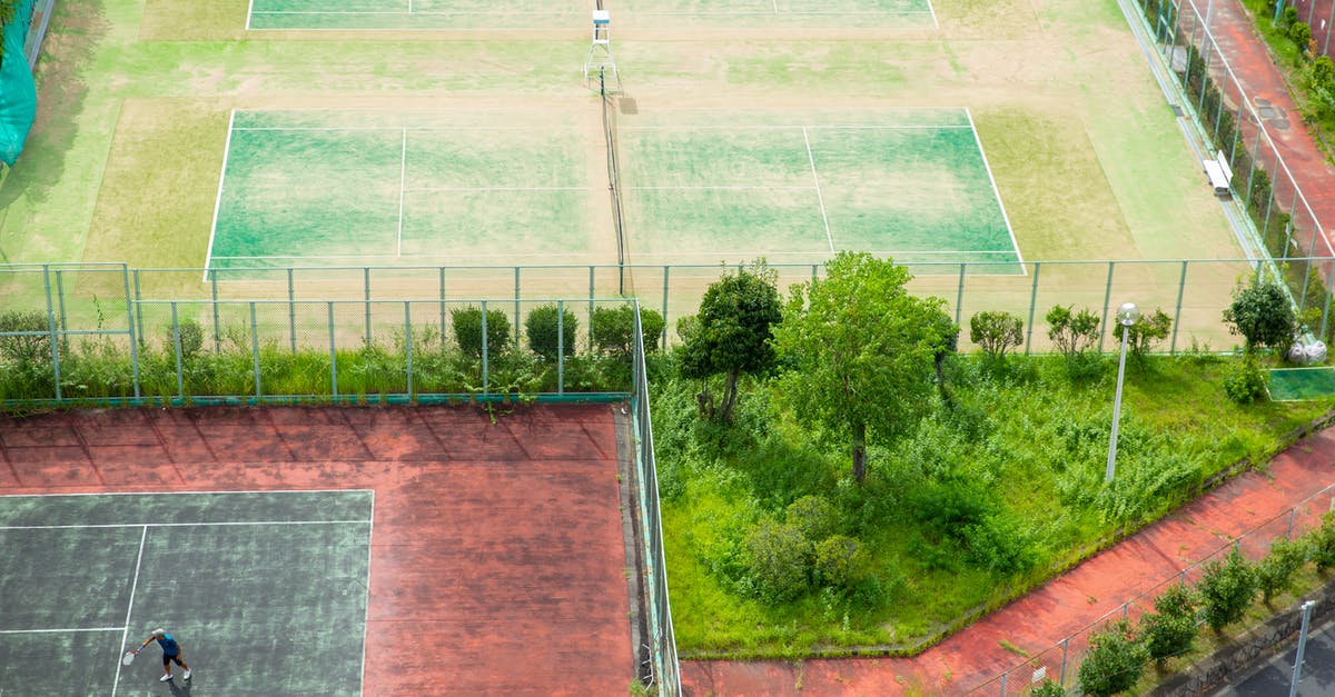 Tennis courts inside or near Kruger National Park - Aerial view of distant person playing tennis on aged weathered tennis courts on lush green meadow