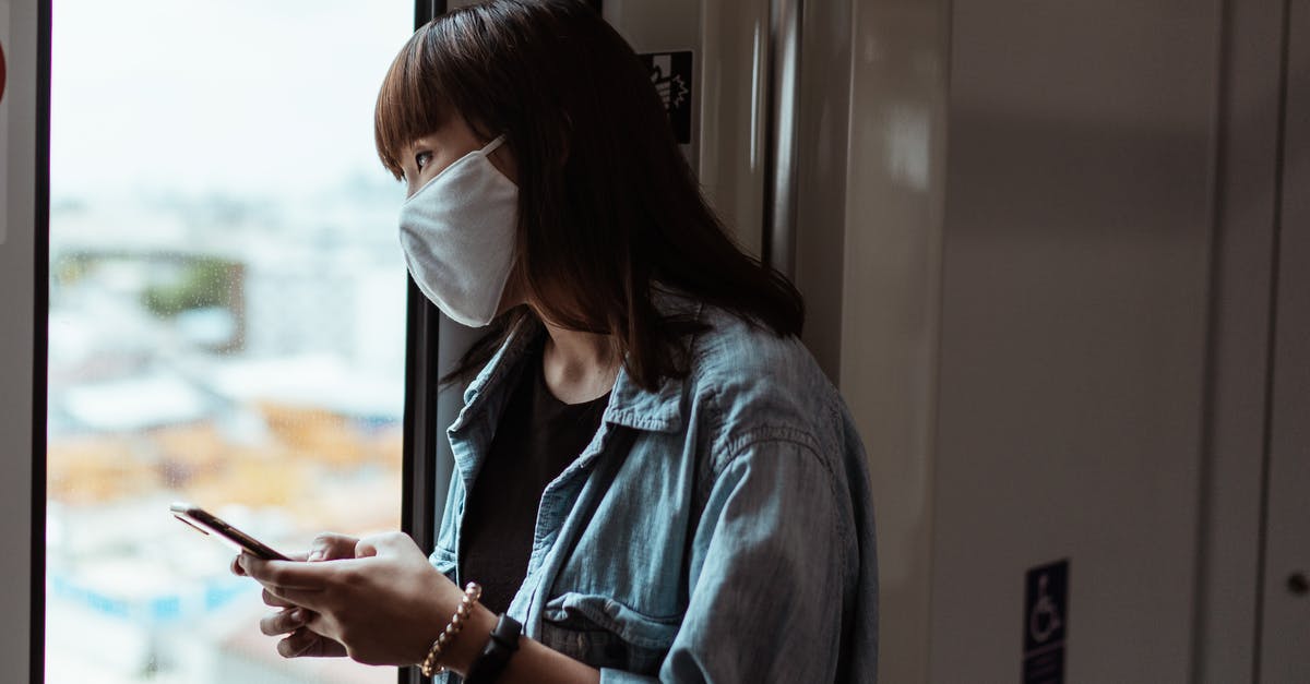 Texting someone who is out of the country? - Woman Wearing a Face Mask and Holding a Smartphone