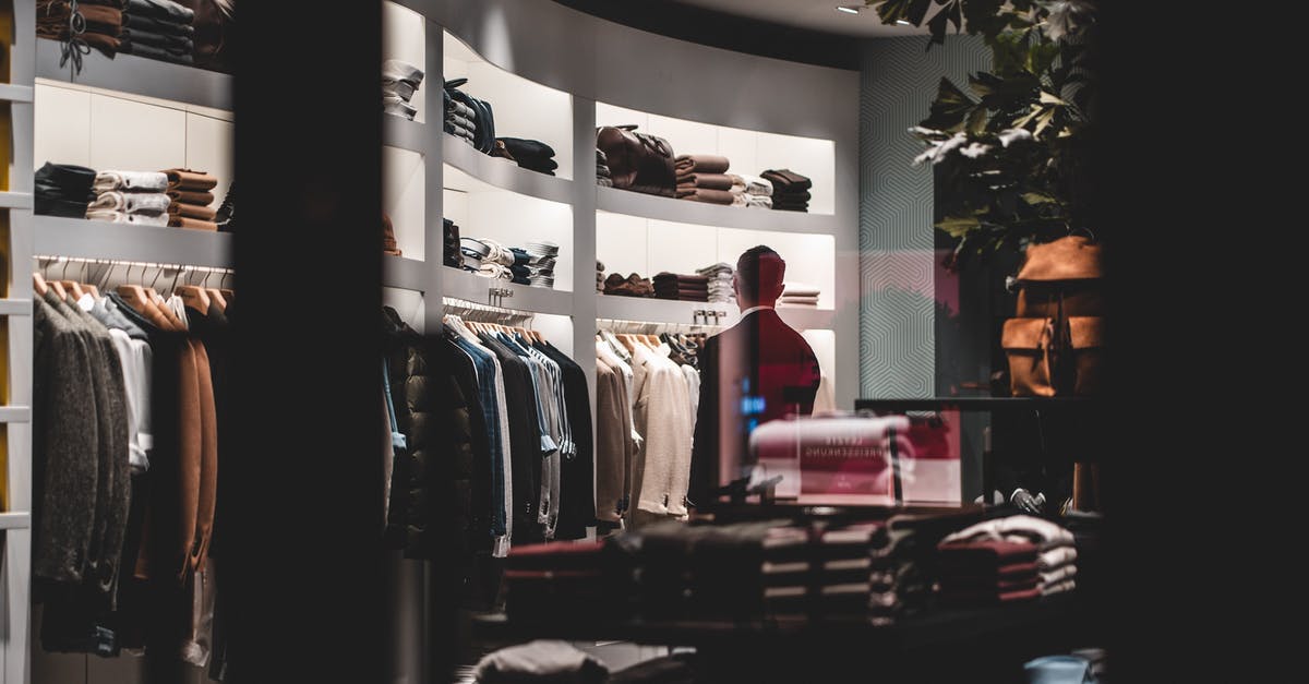 Time for Visa collection after the decision - Back view of faceless elegant male customer in suit choosing new clothes while standing near wardrobe in modern fashion boutique