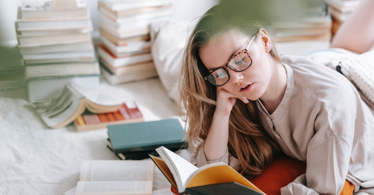 Time left on an ESTA [duplicate] - Concentrated young female in eyeglasses reading book while lying on white blanket near heap of literature in light room at home