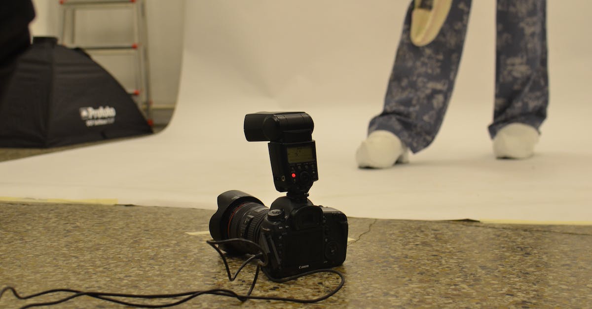 Tool to capture all my travels? - Professional modern photo camera with flash placed on floor in studio against crop faceless model