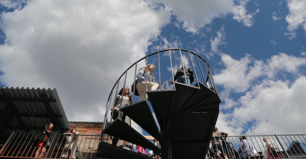 Tourist / simple city maps to print - From below of people on spiral stairway and building terrace with railing under cloudy blue sky in daytime