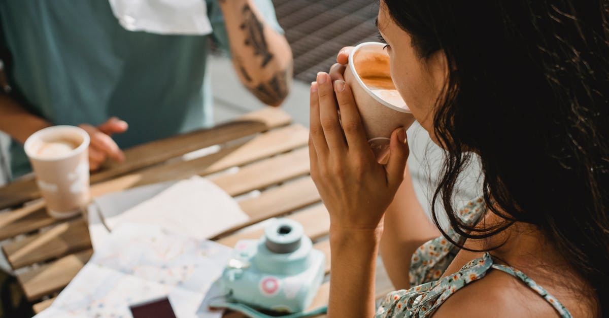 Tourist guide for self-made holiday [closed] - From above of crop anonymous couple drinking coffee while sitting at table with map and instant photo camera during vacation together