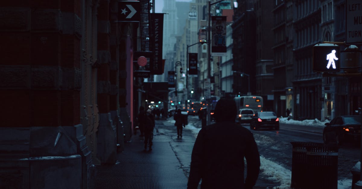 Tourist Kuwaiti visa requirements for a Bangladeshi citizen - Back view of anonymous pedestrian strolling on asphalt sidewalk on street of city with high buildings during traffic jam hour in winter at twilight