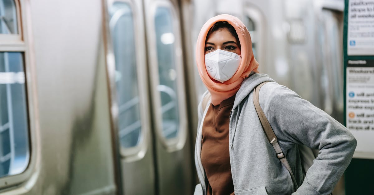 Train from Zurich to Salzburg and February 2022 COVID restrictions - Young Muslim female in casual wear and traditional headscarf with protective mask on subway platform