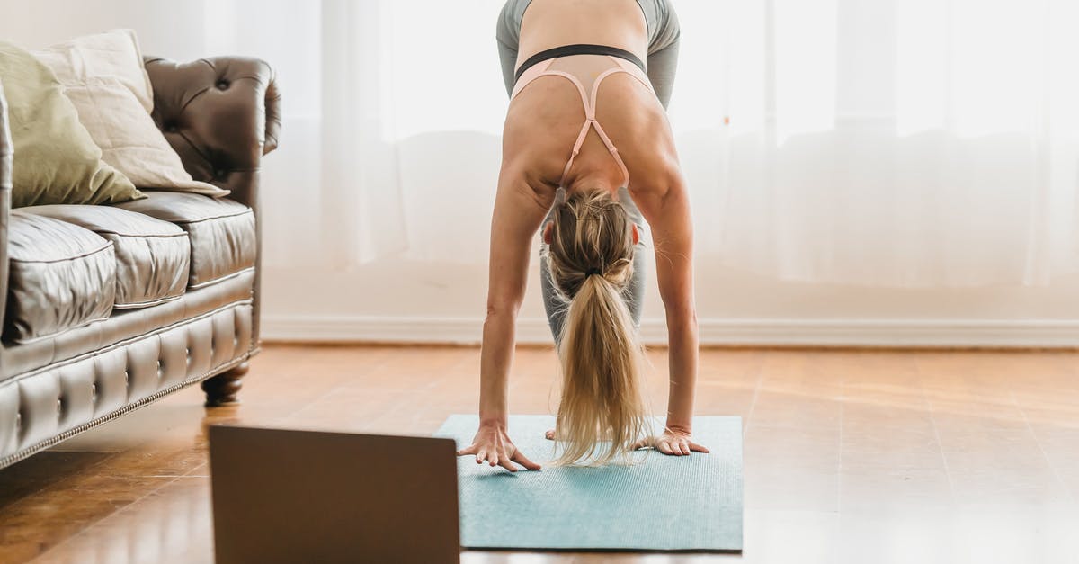 Trains connections between Cannes and Montpellier - Full body of unrecognizable female in activewear performing standing forward bend asana while standing on mat near laptop during online yoga lesson at home