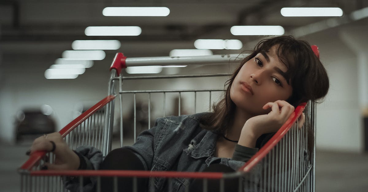 Transit accessible parking lots near Amsterdam - Dreamy female with black hair and head tilted to side with hand near face sitting in metal cart while looking at camera on blurred underground parking lot