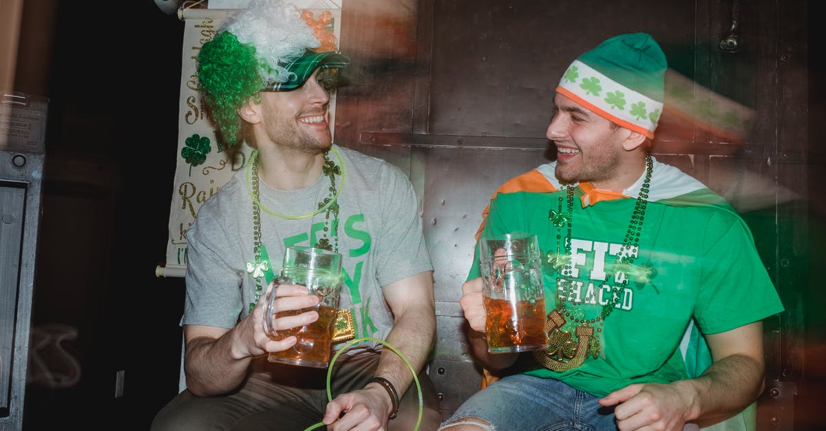 Transit through UK with Irish visa - Through glass wall view of smiling male partners with mugs of beer looking at each other during Feast of Saint Patrick