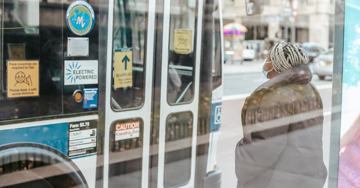 Transiting through Netherlands in private vehicle during Covid restrictions - Through glass wall back view of anonymous ethnic female medic standing against public transport in town