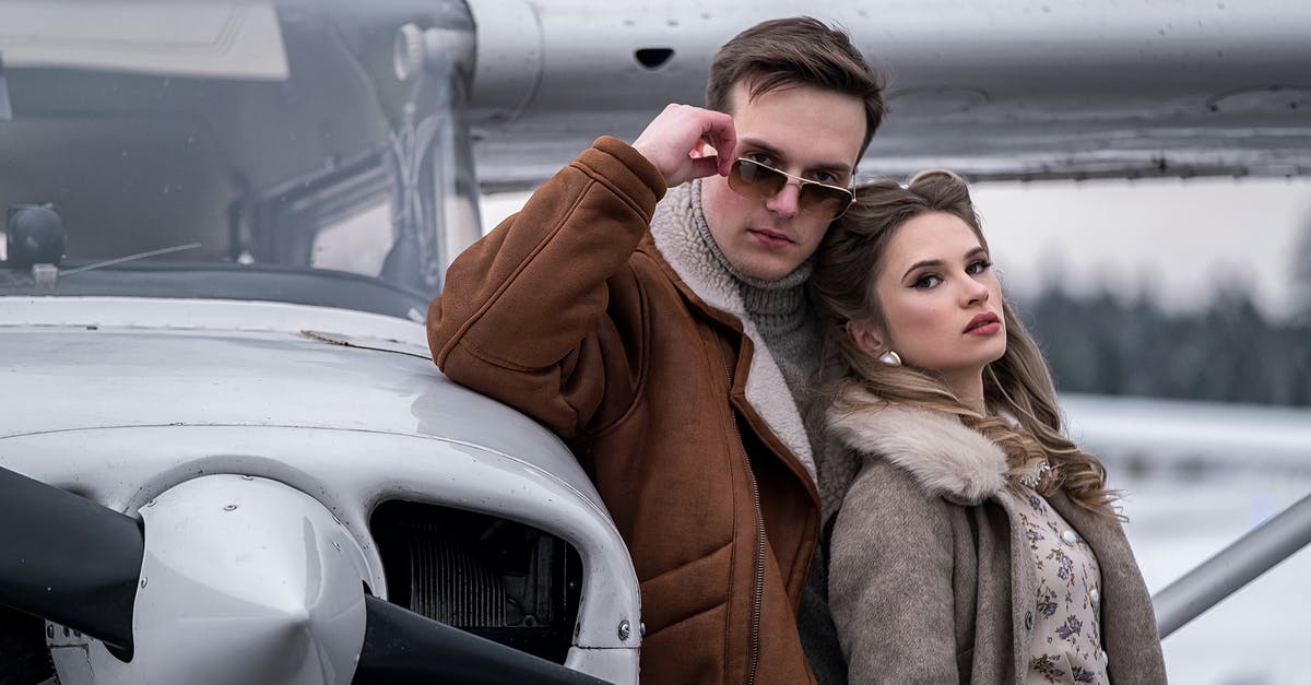 Transport from Frankfurt Hahn Airport [closed] - Young couple in trendy warm wear standing close near turboprop airplane on winter airfield and looking at camera