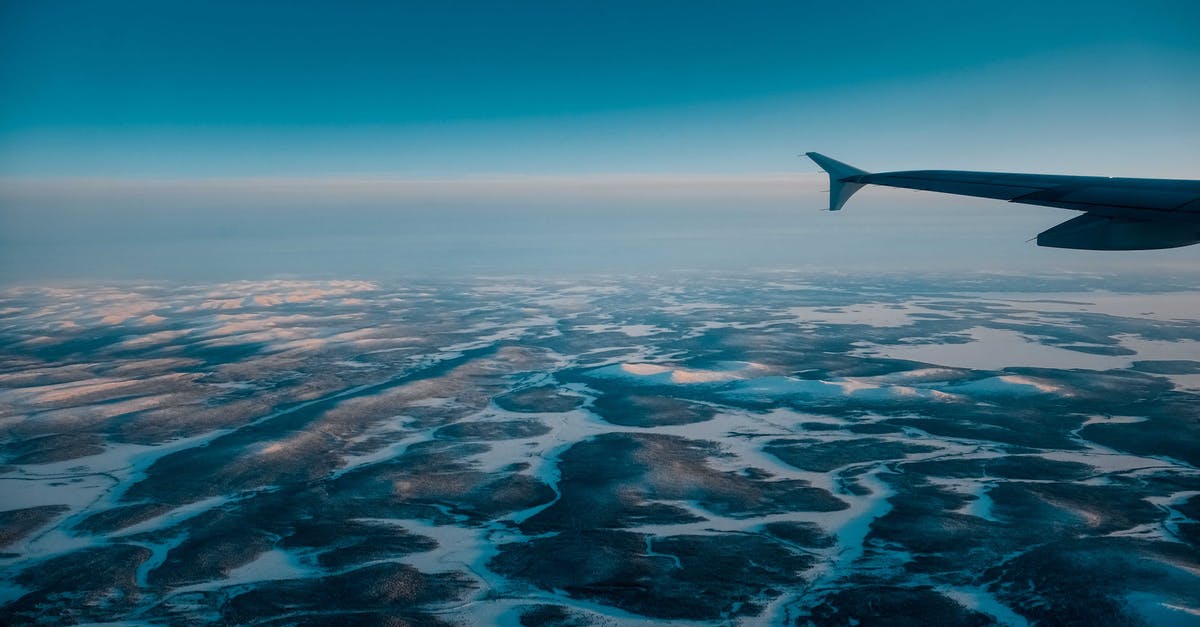 Transport frozen mother's milk by plane - Wing of airplane flying in blue cloudless sky with skyline above vast terrain covered with snow in nature on winter day