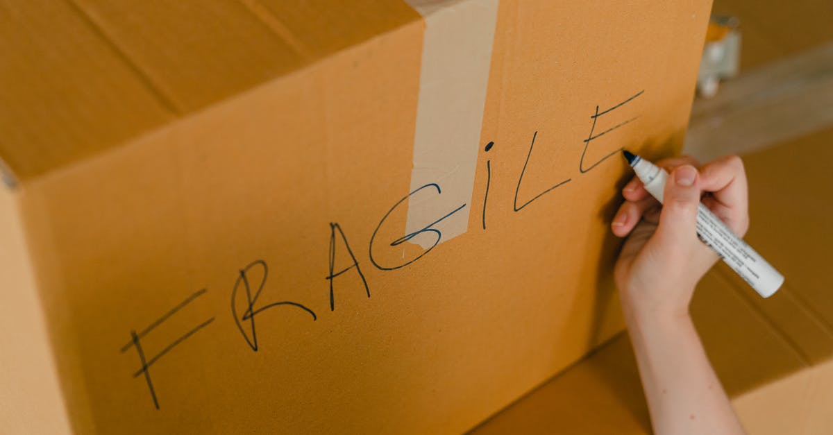 Transporting fragile ceramics in carry-on with Ryanair - From above of crop unrecognizable person writing with marker on cardboard box with fragile products before relocation