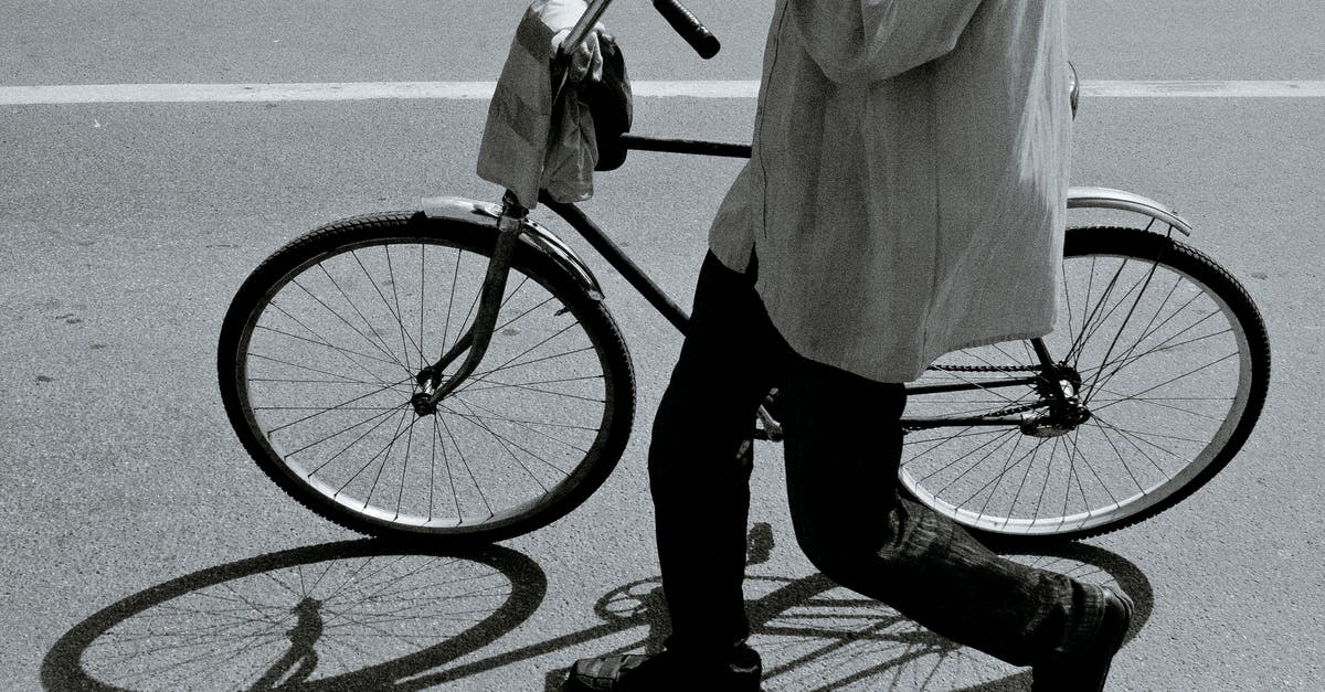 Transporting (not riding) a tandem bicycle from Tangier to Essaouira - Side view of black and white crop anonymous person in stylish outfit walking on asphalt road with bicycle on sunny day