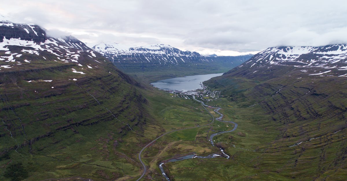 Travel between Heathrow terminals - Spectacular aerial view of narrow river flowing into lake between green slopes of mountains with snow caps under overcast sky