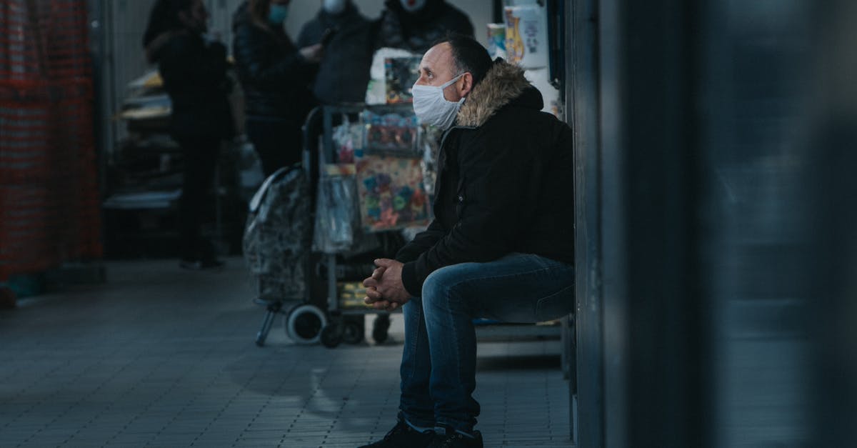 Travel protection bag OK at airport? - Side view of male in warm clothes and mask sitting in public place