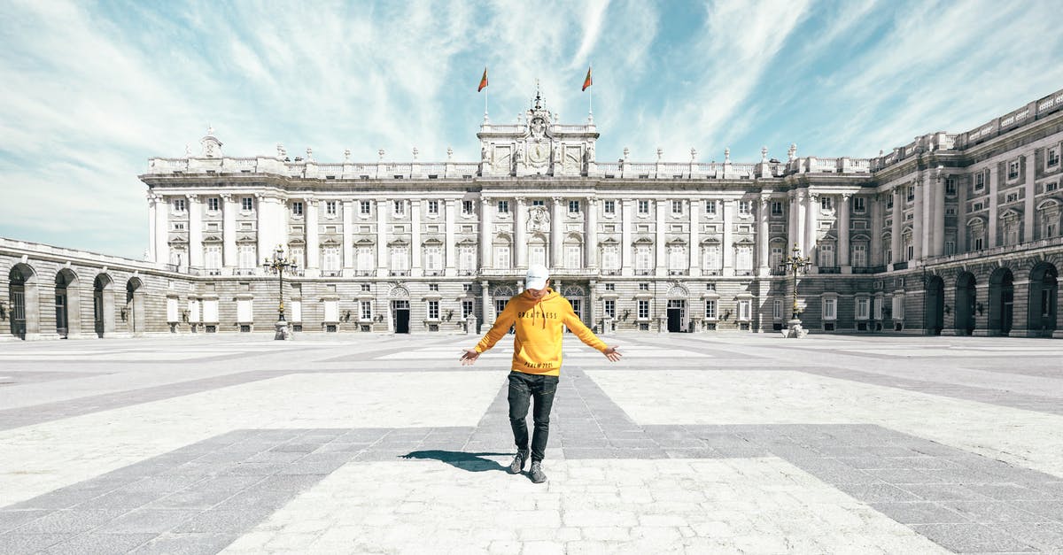 Travel to Spain full vaccinated with a Russian vaccine - Full body of unrecognizable male traveler in casual clothes and cap standing on empty square near Royal Palace of Madrid during holiday in Spain