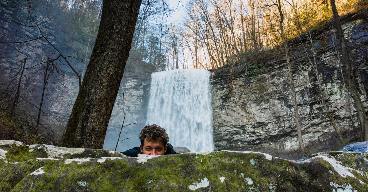 Travel to US - PCR or lateral flow? - Young male hiker hiding behind boulder near waterfall in forest