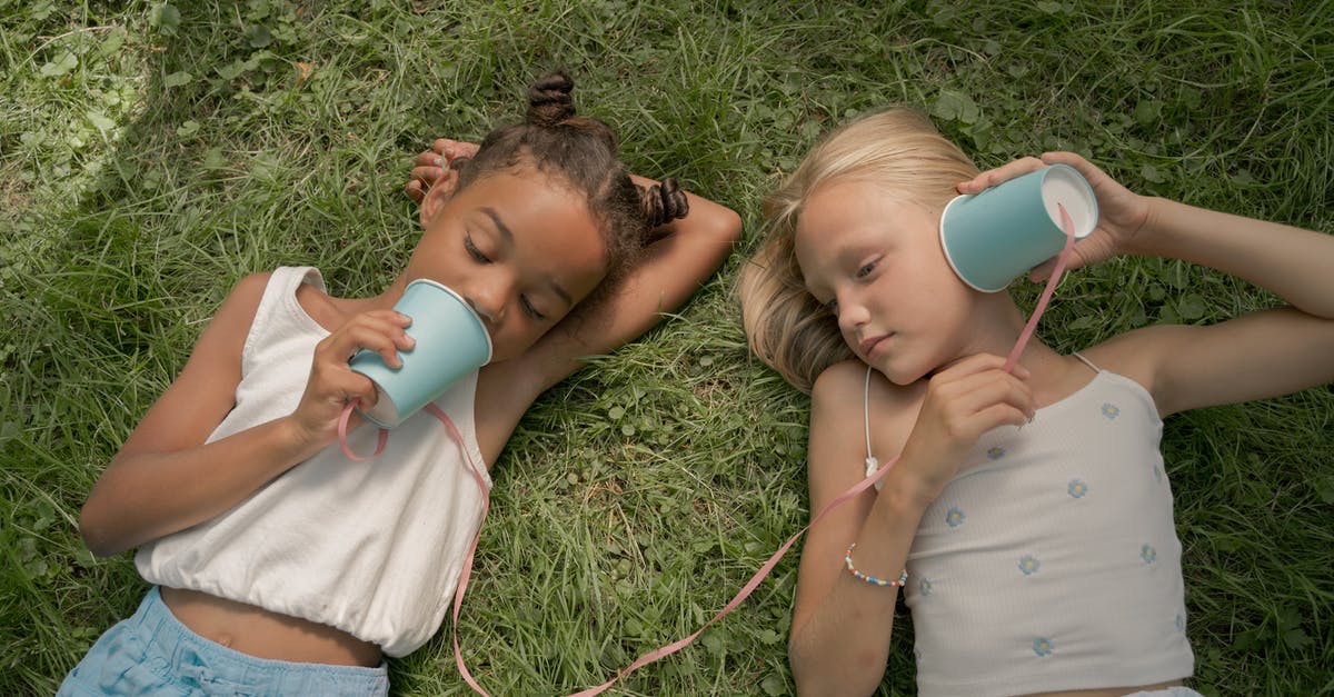 Traveling between Canada and China using two passports [duplicate] - Two Teenage Girls Laying on Grass and Playing Telephone Call Using Paper Cups on String