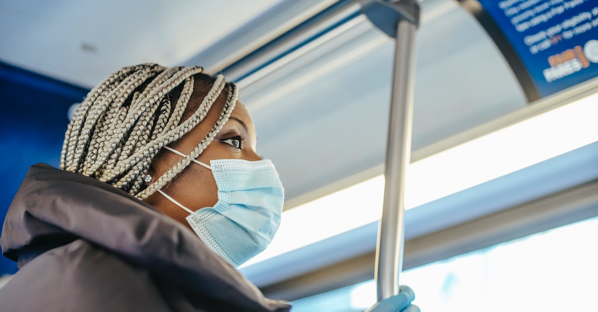 Traveling from San Francisco to Tokyo with a peculiar medical condition - From below side view of African American female medic in disposable glove and mask looking forward in public vehicle