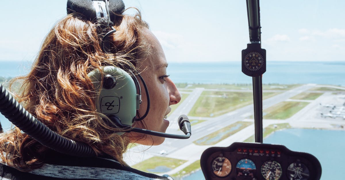 Traveling inside Schengen without a ticket to fly back home (Venezuela) - Back view of positive young female traveler in casual wear and headset sitting in cockpit of modern helicopter during flight over coastal town