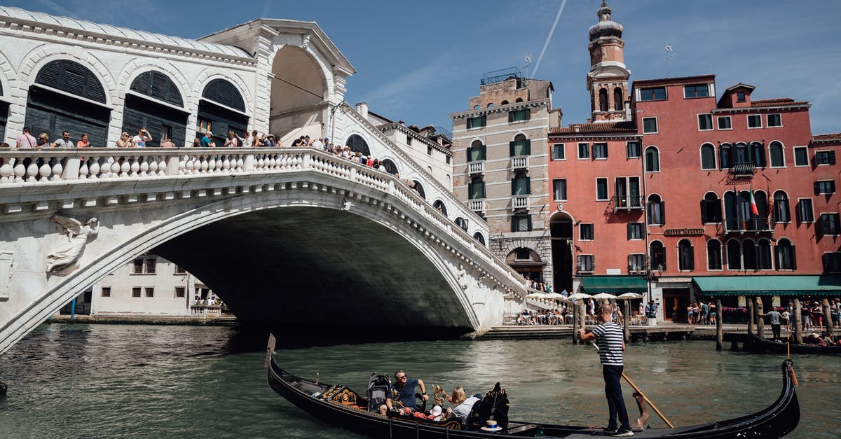 Traveling outside Italy with permesso di suggorno - Travelers floating on gondola on Grand canal near famous bridge among aged residential buildings in Venice during vacations in Italy