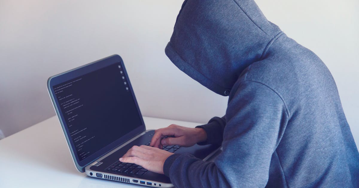 Traveling to a country known for mass surveillance. How can I protect my data/privacy? - Side view of unrecognizable hacker in hoodie sitting at white table and working remotely on netbook in light room near wall